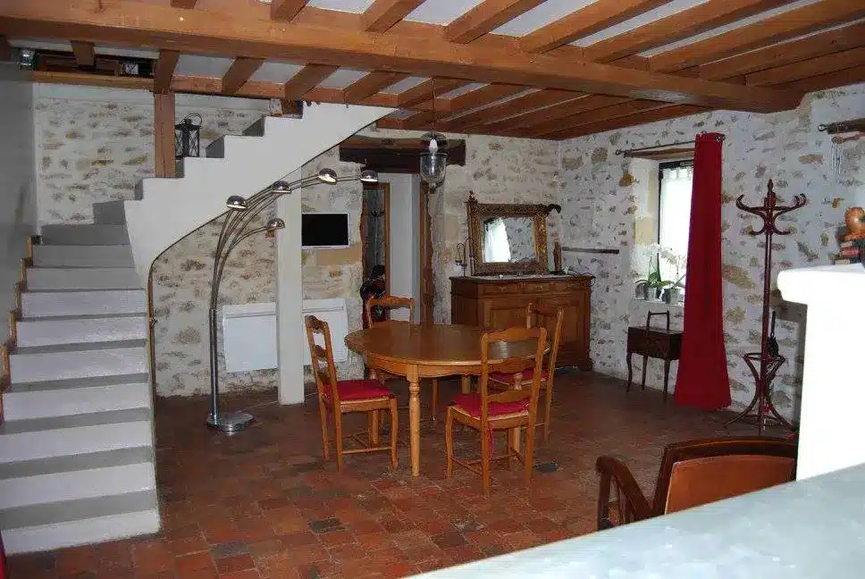 Intérieur d'une cuisine de gîte de charme, table et chaises en bois, sol en tomettes, décor convivial et rustique.